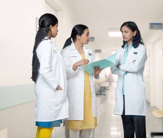 Dr Vani Sundarapandian and two Jananam colleagues reading a case file together in the corridor at Jananam Fertility Centre, Neelankarai, Chennai