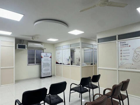 The patient waiting area at Jananam Fertility Centre, Thiruporur, with rows of chairs under a ceiling fan and a glazed reception window